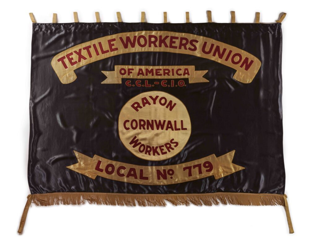 A shiny, black banner with a gold fringe along the bottom and gold tabs along the top, red text in decorative gold scrolls and a central gold circle relating to the TEXTILE WORKERS UNION, its affiliations, workers and local.