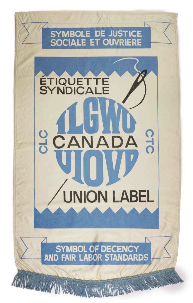 A discoloured long, vertical, white banner with a blue fringe across the bottom, and text in blue and black relating to ILGWU union, and what the union, and the label on the banner, symbolize, an image of a needle and thread crosses behind the logo in the centre.