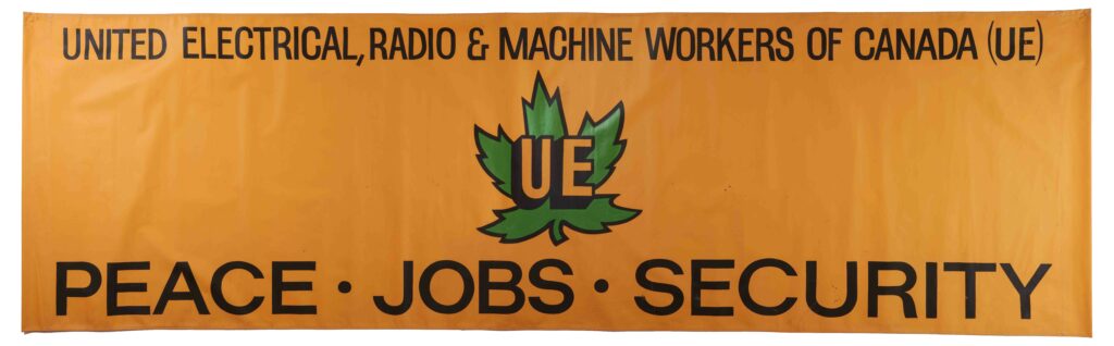 Long horizontal orange banner with words across the top in black UNITED ELECTRICAL, RADIO & MACHINE WORKERS OF CANADA (UE), and across the bottom PEACE • JOBS • SECURITY, a green maple leaf in the middle with the initials UE across it
