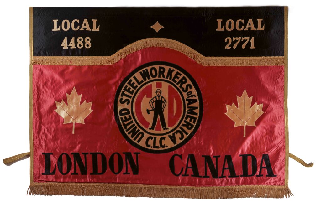 A banner made of shiny fabric, most of the background is red with a black band across the top with LOCAL 4488 and LOCAL 2771 on each side in gold, across the bottom LONDON CANADA, in the middle a logo with union initials and a standing workman, each side of the logo is a gold maple leaf