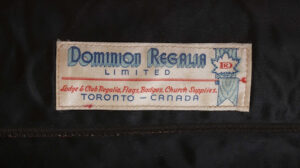 Label with text in blue and red and a maple leaf against a ribbon, in the style of a rosette