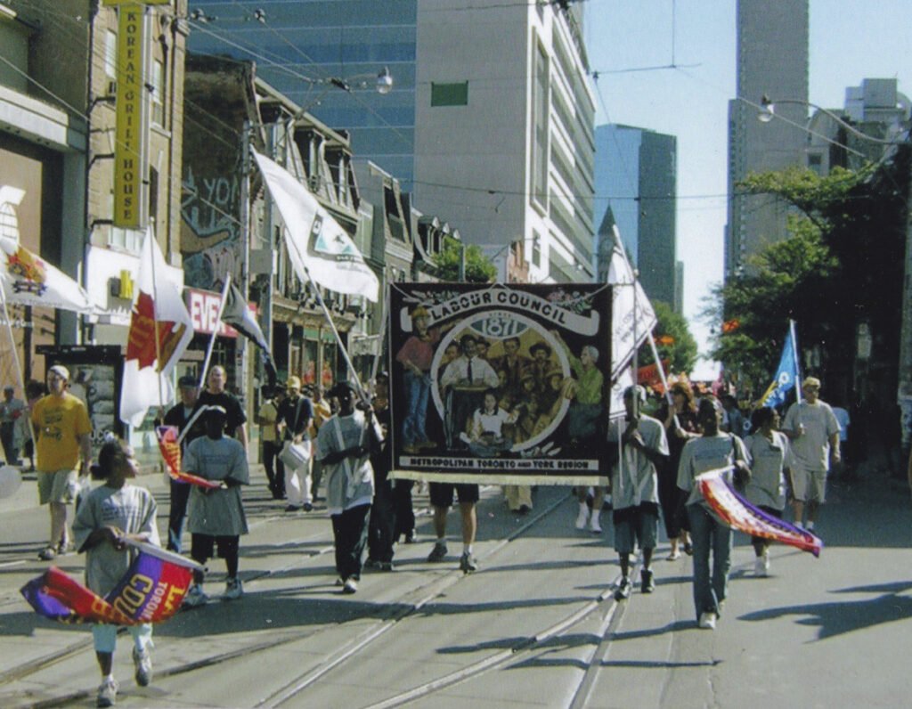 Colour photo of a parade, many people carrying flags and banners
