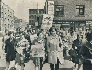 Black and white photo of women demonstrating in the street, some are holding placards