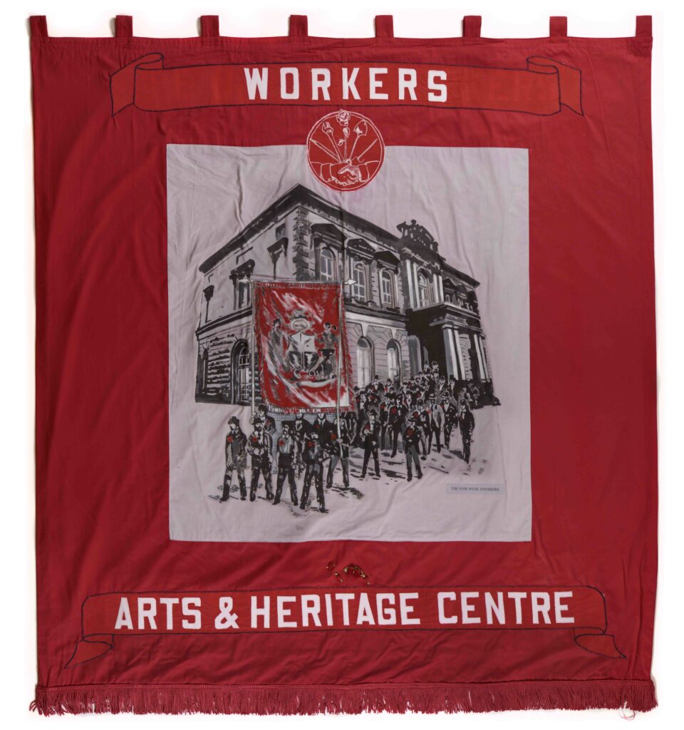 Red banner, central grey panel with illustration of large Victorian building with parade of people outside, holding at the front a red banner, at the top and bottom of the panel is white text, below the text at the top is a red and white logo of two shaking hands under a range of tools